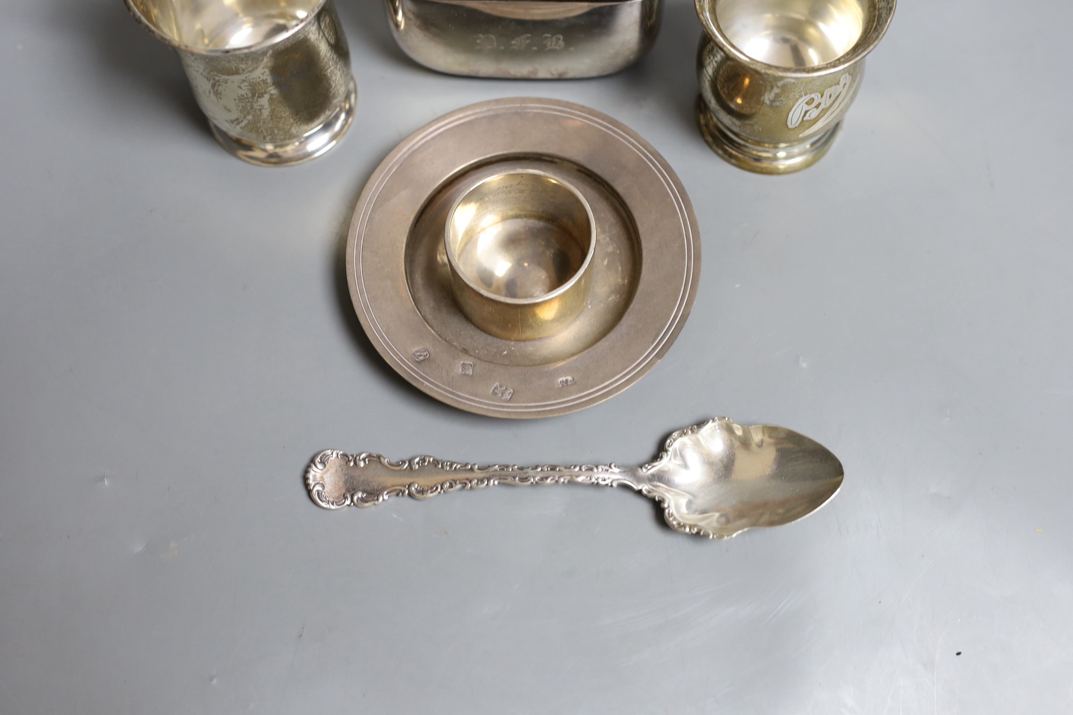 Two small George V christening mugs, a small modern silver armada dish, a silver napkin ring, ornate silver spoon and a silver plate and leather mounted glass hip flask.